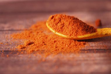 Tahtadaki sarı kaşıkta renkli kırmızı bir toz duruyor..