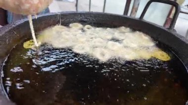 Hamur halkaları, hareketli bir sokak mutfağında kızgın yağda kızartılıyor..