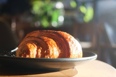 Sıcak bir kafe atmosferinde, koyu bir tabakta taze pişmiş kruvasan..