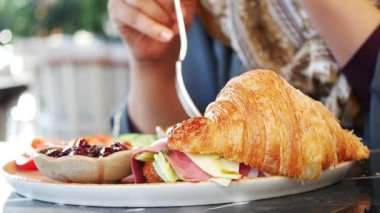 Güneşli bir kafede lezzetli bir kruvasan sandviçi yiyorum.,