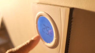 Bir kişi oda sıcaklığını ayarlamak için termostatı ayarlıyor..