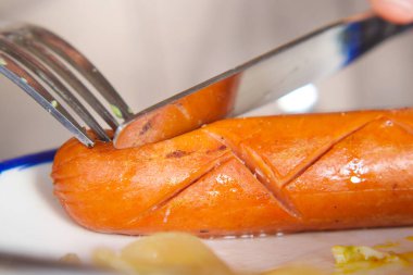 Yemek sırasında ızgara sosis dilimlemek için çatal ve bıçak kullanılır..