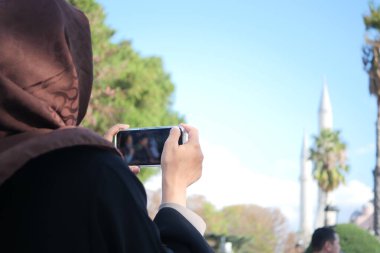 Kafiyeli bir kadın camiyi ele geçirmek için akıllı telefonunu kullanır..