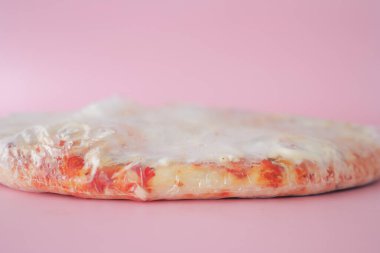 Pembe bir arka fonda duran şeffaf plastiğe sarılı lezzetli pizza..