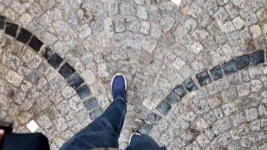 Kişi sakin bir alanda mavi ayakkabıyla kaldırım taşında yürür..