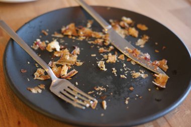 Siyah bir tabakta, çatal bıçaklarla tatminkar bir yemeğin kalıntıları..