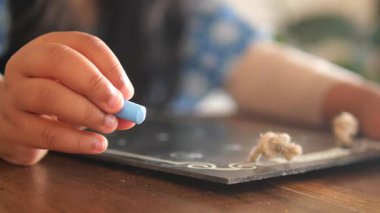 Bir çocuk siyah karatahtaya mavi tebeşir çizer..