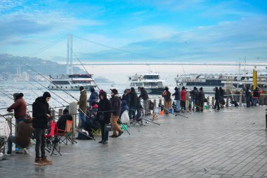 Balıkçılar rıhtımda kuyruk oluşturuyorlar, tekneler yakınlardan geçerken..