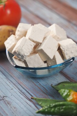Taze sebze ve meyvelerle çevrili bir kasede dilimlenmiş tofu..