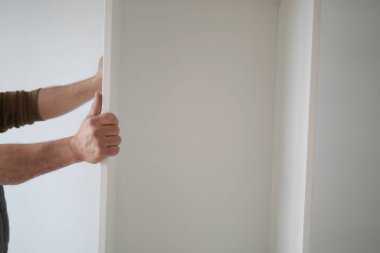 Bir insan minimalist alanda beyaz bir raf paneli ayarlar.