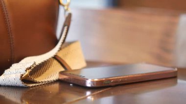 Bir akıllı telefon, sakin bir ortamda şık bir el çantasının yanında bir masanın üzerinde yatar..