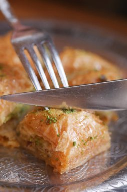 Bir insan süslemeli bir tabakla bir parça baklava keser..