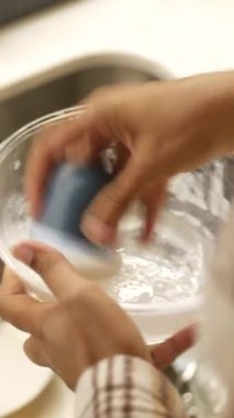 Elleri bir mutfakta akan suyun altındaki tabağı ovalıyor..