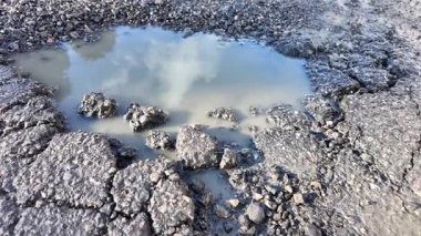 Hasarlı asfalt içinde büyük bir su birikintisi oluşturur ve bulutları yansıtır..