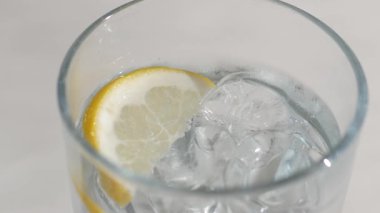 Buzlu suyla dolu bir bardak ve üzerinde bir dilim limon yüzüyor..