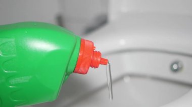 Birisi yeşil şişeden klozete tuvalet temizleyicisi sürüyor..