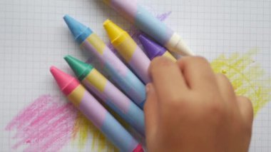 Bir çocuk grafik kağıdını neşeyle boyamak için parlak boya kalemleri kullanır..