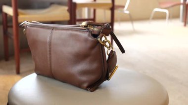 Kahverengi deri bir çanta zarif bir şekilde bir taburede oturuyor, tasarımını sergiliyor..