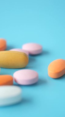 Mavi bir yüzeye dağılmış çeşitli renkli vitaminler ve takviyeler..