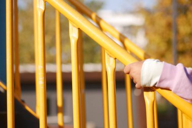 Bir çocuk, çocuk parkındaki merdivenleri çıkarken sarı korkuluklara tutunuyor..