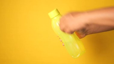Bir el zarif bir şekilde sarı bir arka fonun önünde parlak sarı bir şişe tutar..