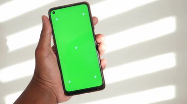 Bir insan güneş ışığında yeşil ekranlı bir akıllı telefon tutar..