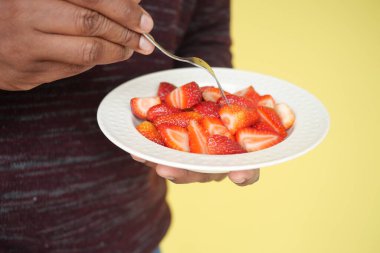 Birisi elinde çatalla taze kesilmiş çilek tabağı tutuyor..