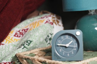 Kaliteli bir saat, yeşil bir lambanın yanında, rahat bir sepetin üzerinde durur..