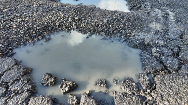 Son yağmurun ardından hasarlı bir yol yüzeyinde su birikiyor.