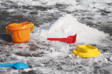 Renkli oyuncak kovaları ve kürekler dışarıda köpüklü karların üzerinde dinleniyor..