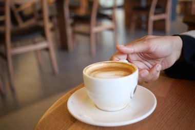 Bir kafede dinlenirken dumanı tüten bir fincan kahve tutan bir el..