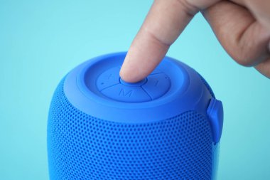 Bir el mavi taşınabilir bir hoparlörün kontrol paneliyle etkileşime girer..