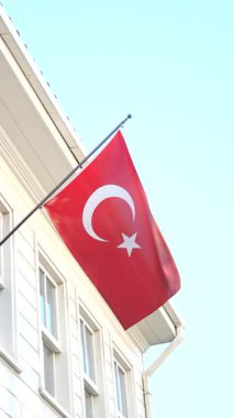 Canlı bir Türk bayrağı parlak gökyüzünün altında rüzgarda belirgin bir şekilde dalgalanıyor.