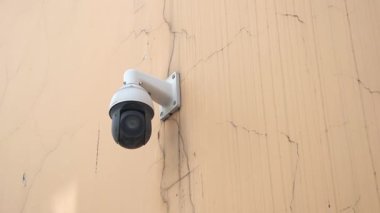 Bir güvenlik kamerası yıpranmış bir duvardan bölgeyi izliyor..