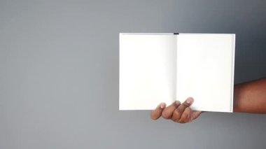 Bir kişi gri arkaplanı olan boş bir defter gösterir, yaratıcılığı davet eder.