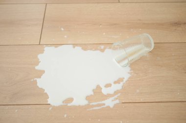 Bir bardak yere devrildi ve süt ahşap yüzeye döküldü..