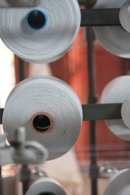Beyaz iplik makaraları bir tekstil fabrikasında makineler üzerinde döner.