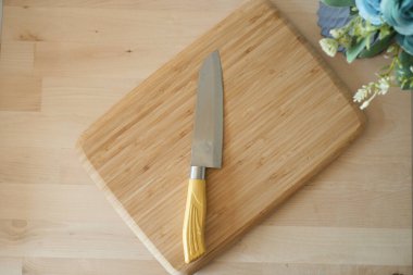 Keskin bir mutfak bıçağı, dekorla çevrili bir bambu kesme tahtasının üzerinde duruyor..