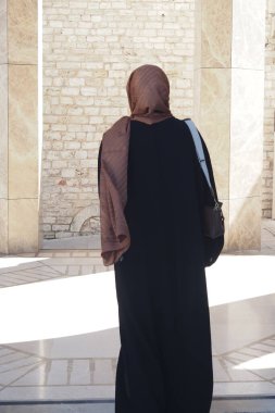 Uzun siyah elbiseli bir kadın eski bir mekanda yürüyor..