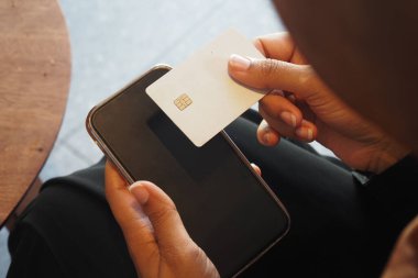 Bir kişi cep telefonundan ödeme yapmak için kart kullanır..