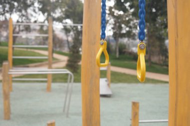 Sarı salıncaklı ve ağaçların altındaki tırmanma çerçeveli sessiz oyun alanı.
