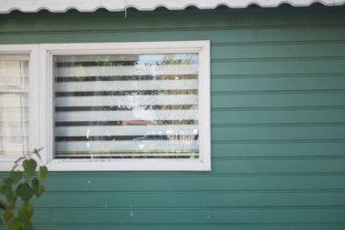 Sessiz bir mahalle evinde yeşil dış ve çizgili perdeler vardır..