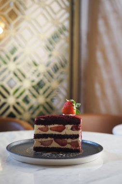 Taze çilekle kaplanmış canlı kırmızı kadife bir pasta zarif bir şekilde duruyor..