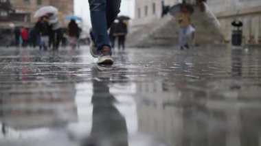 İnsanlar yağmurdan ıslanmış bir sokakta şemsiyeler ardına kadar açık yürürler..