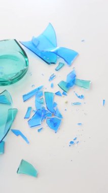 Parçalanmış mavi cam parçaları beyaz bir yüzeye yayılmış..
