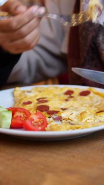 Taze salata malzemeleriyle zenginleştirilmiş omletin tadını çıkaran bir insan..