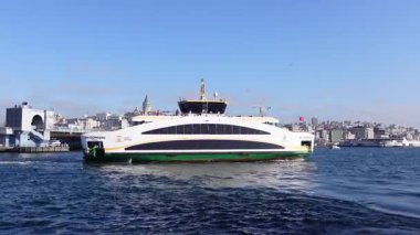 Arka planda Istanbuls silueti olan bir feribot suda hareket ediyor.