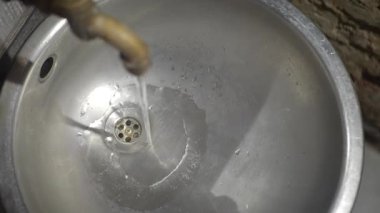 Musluktan temiz su akıntıları yakın çekim görüntüsünde parlak bir lavaboya akıyor..