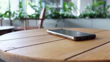 Parlak, yeşil dolu bir odada, ahşap bir masanın üzerinde bir akıllı telefon yatıyor..