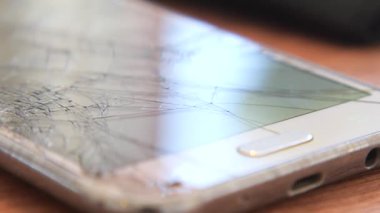 Paramparça bir ekranı olan hasarlı bir akıllı telefon masada oturur..